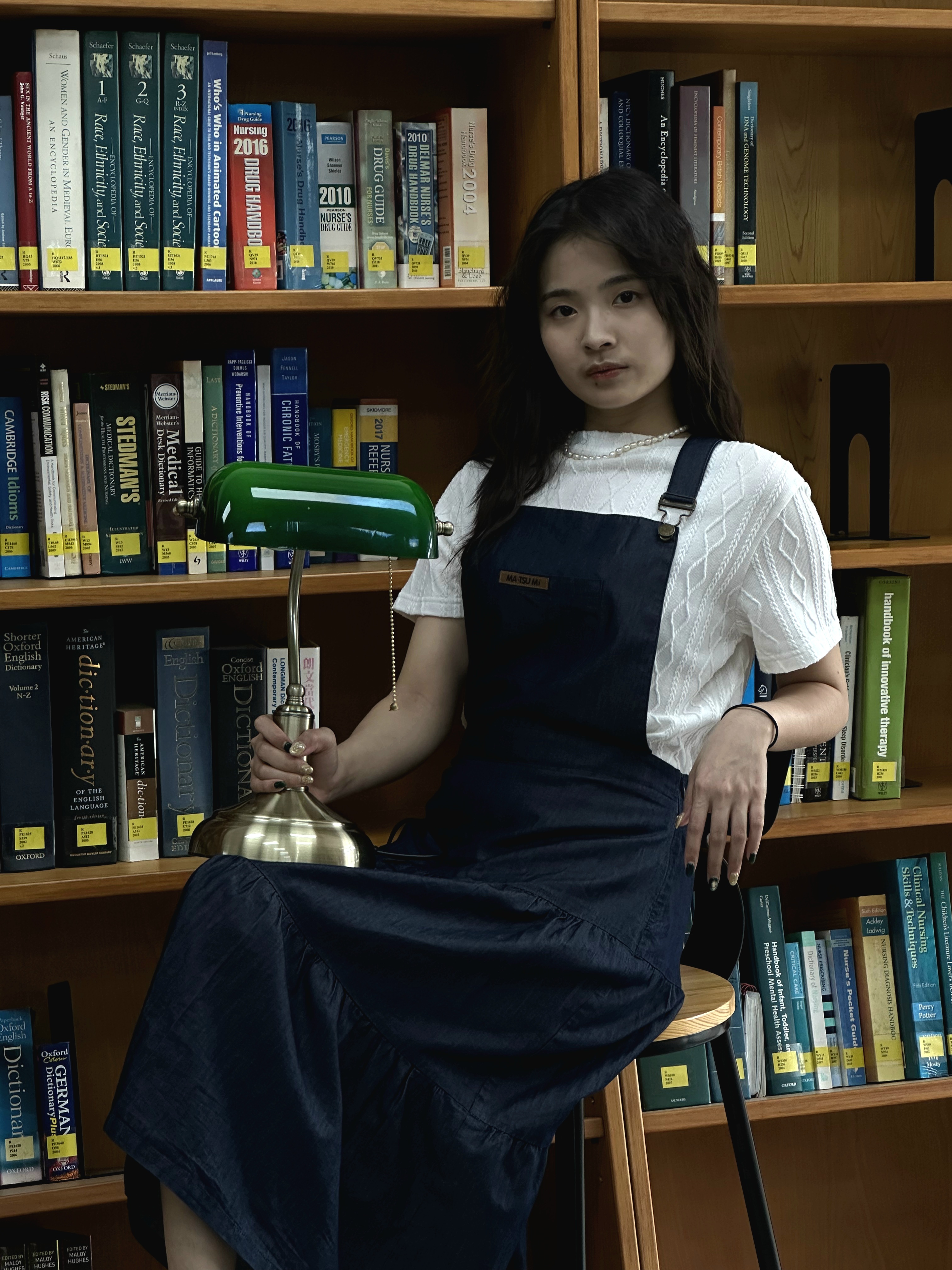 一個女生手拿檯燈坐在書櫃前